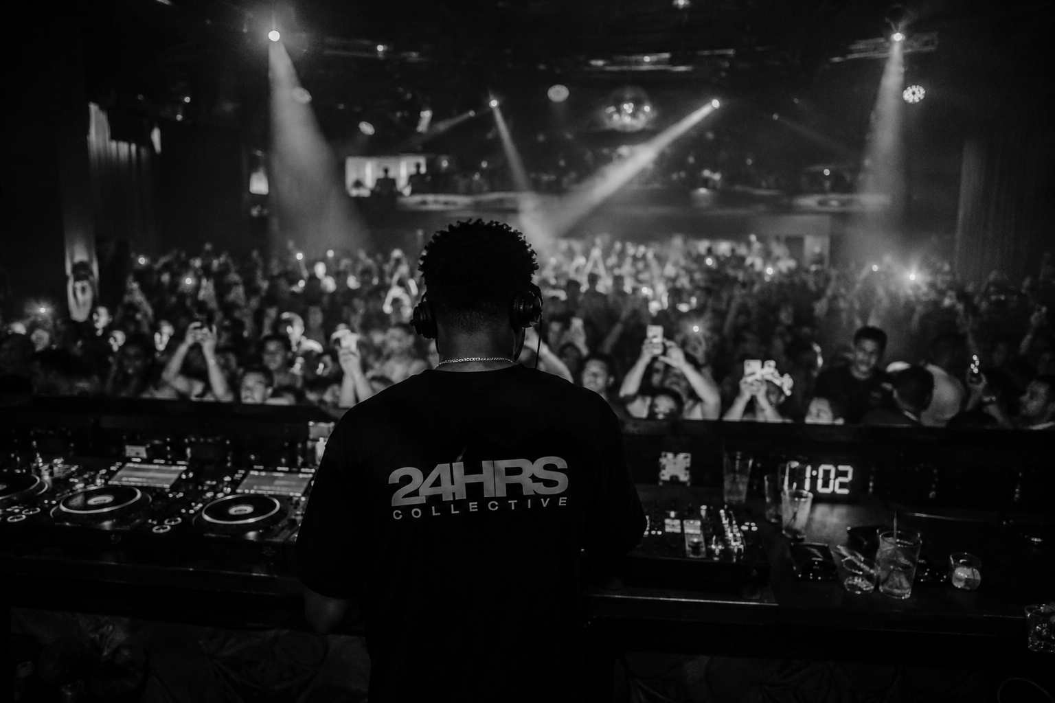 24HRS Collective DJ facing a packed club crowd, shot from behind the booth