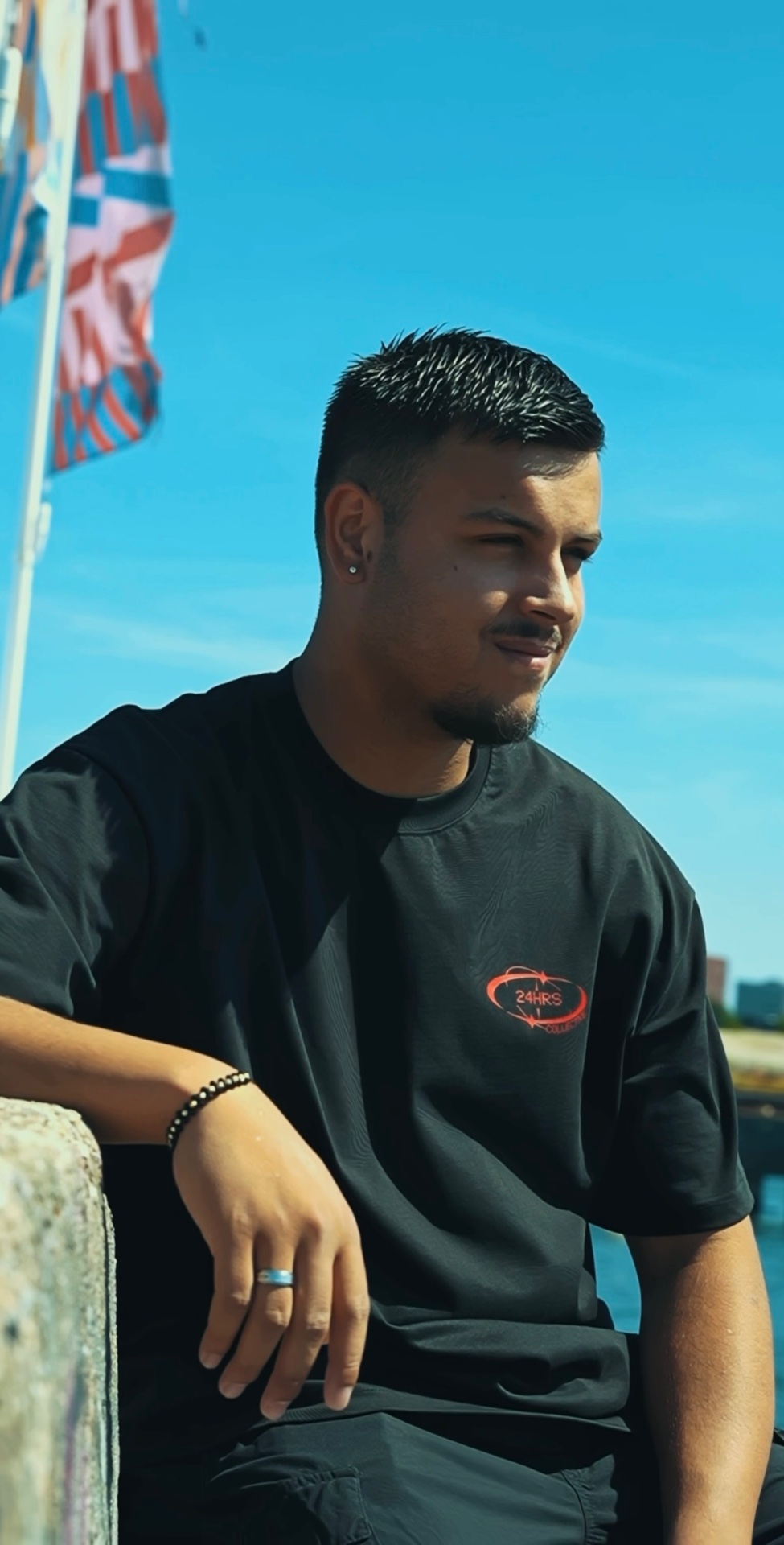 Member of 24HRS Collective wearing the black tee with red logo print by the water
